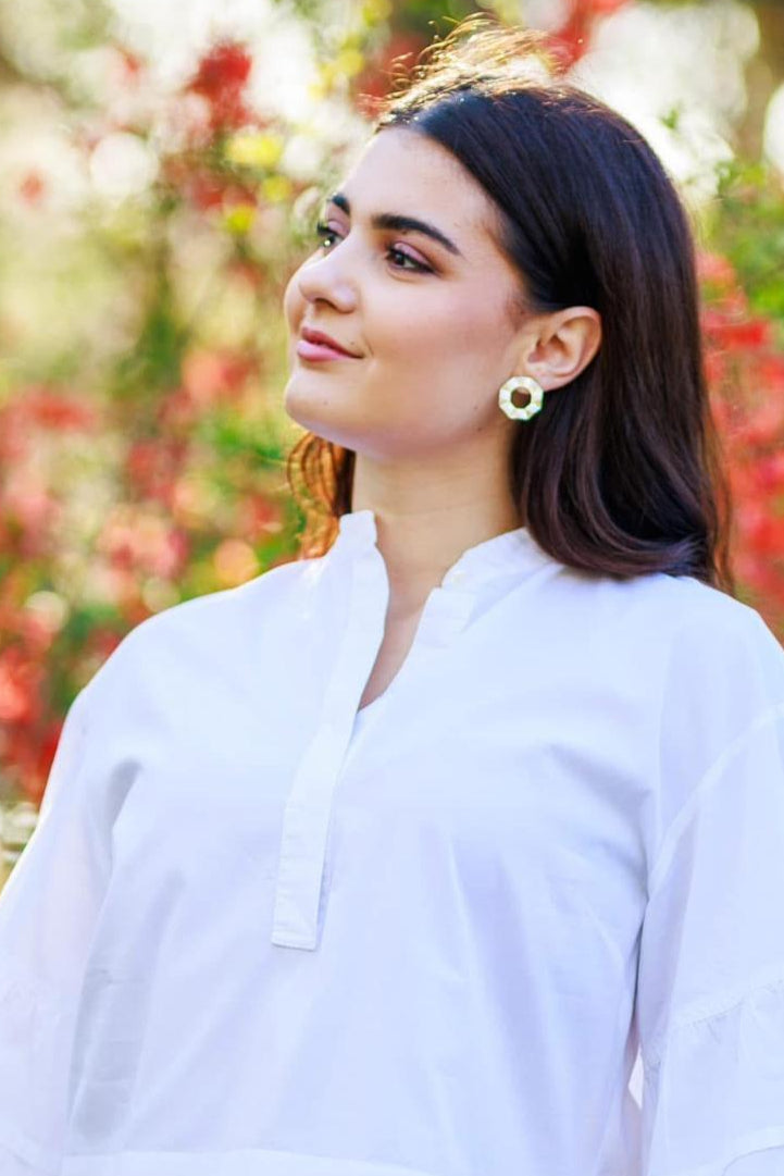 Woman in white blouse with gold earrings, outdoors with colorful blurred background