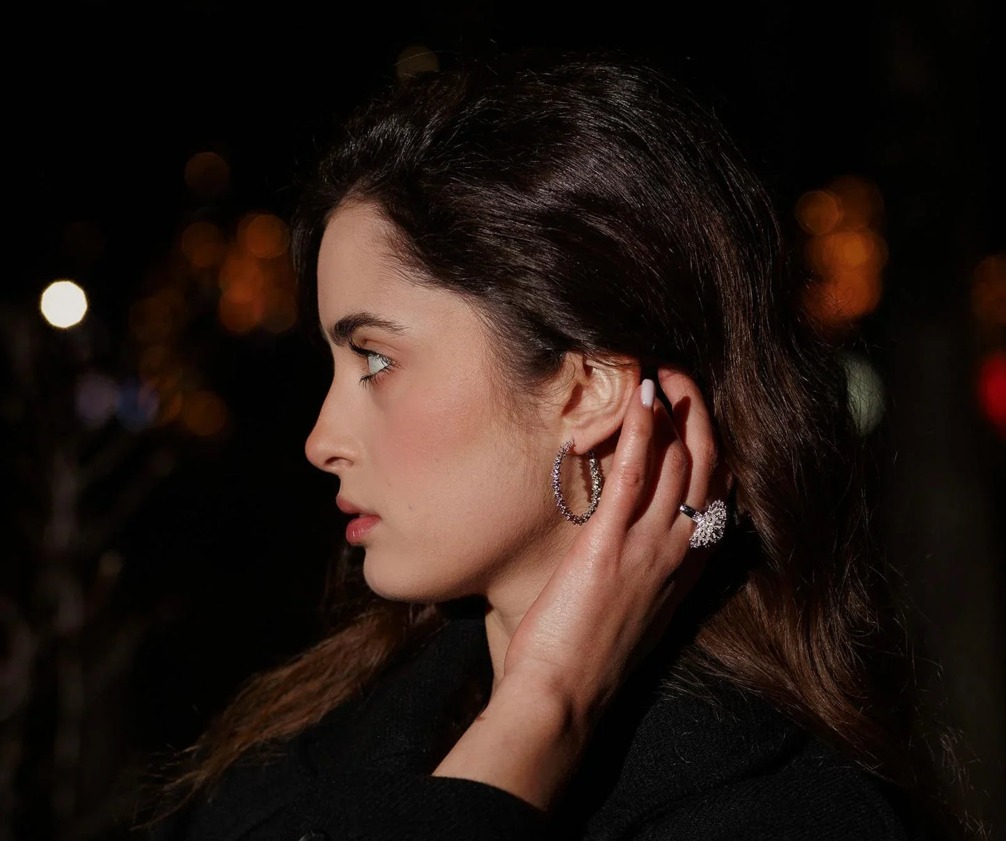 Woman wearing sparkling hoop earrings and statement ring at night