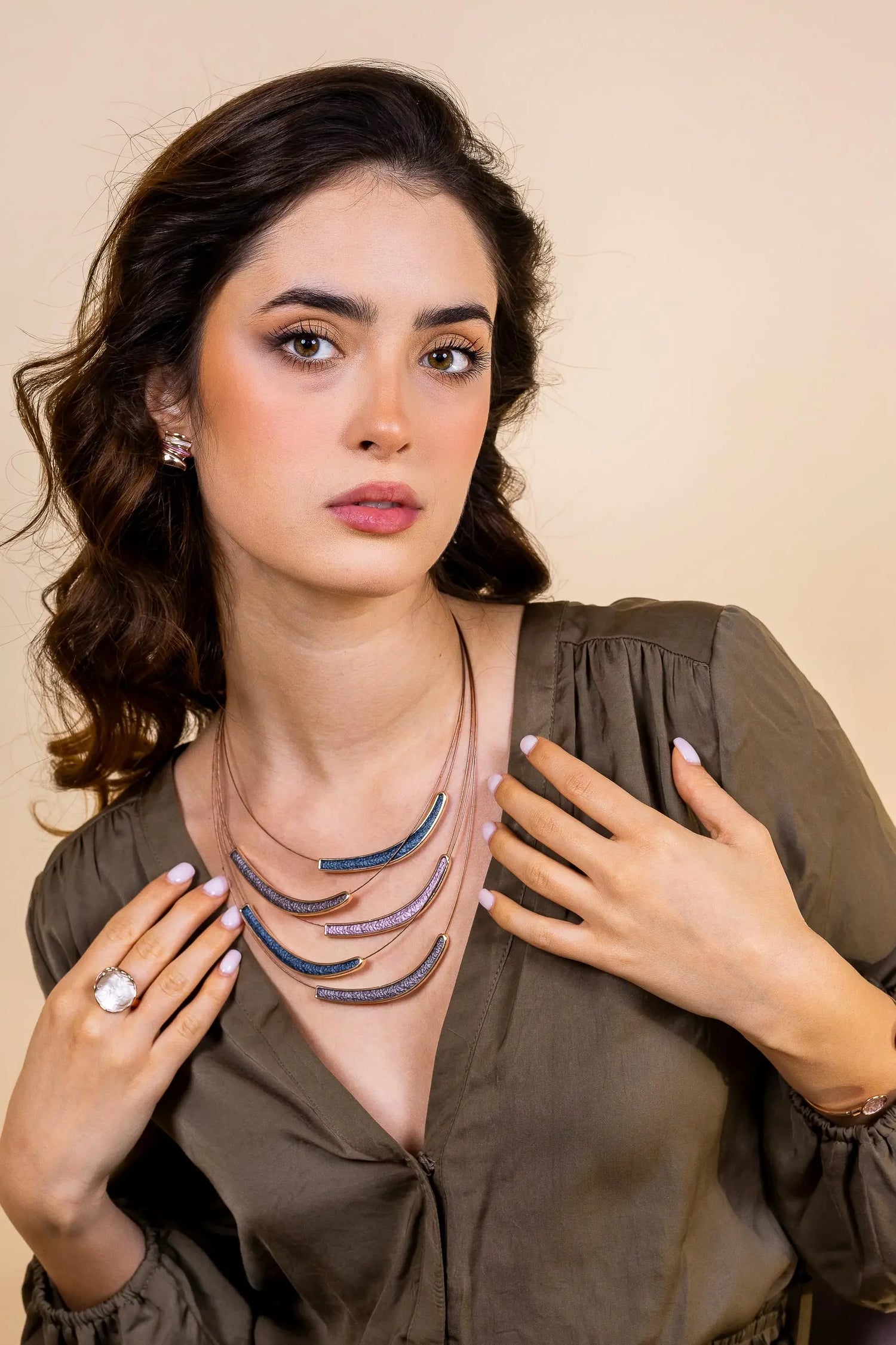 Woman wearing layered statement necklace, stud earrings, and gemstone ring, in green blouse