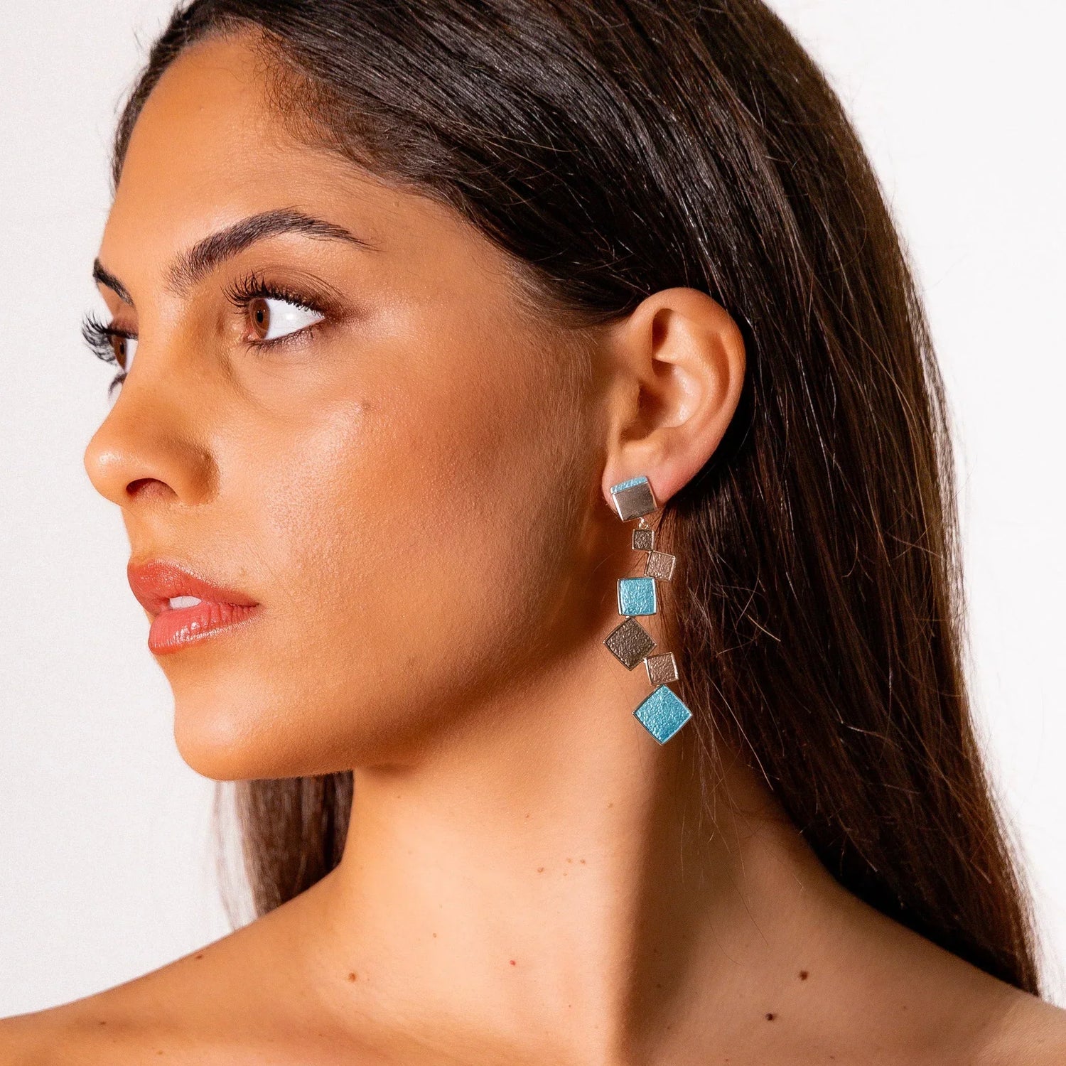 Woman wearing geometric dangle earrings with blue and metallic square shapes
