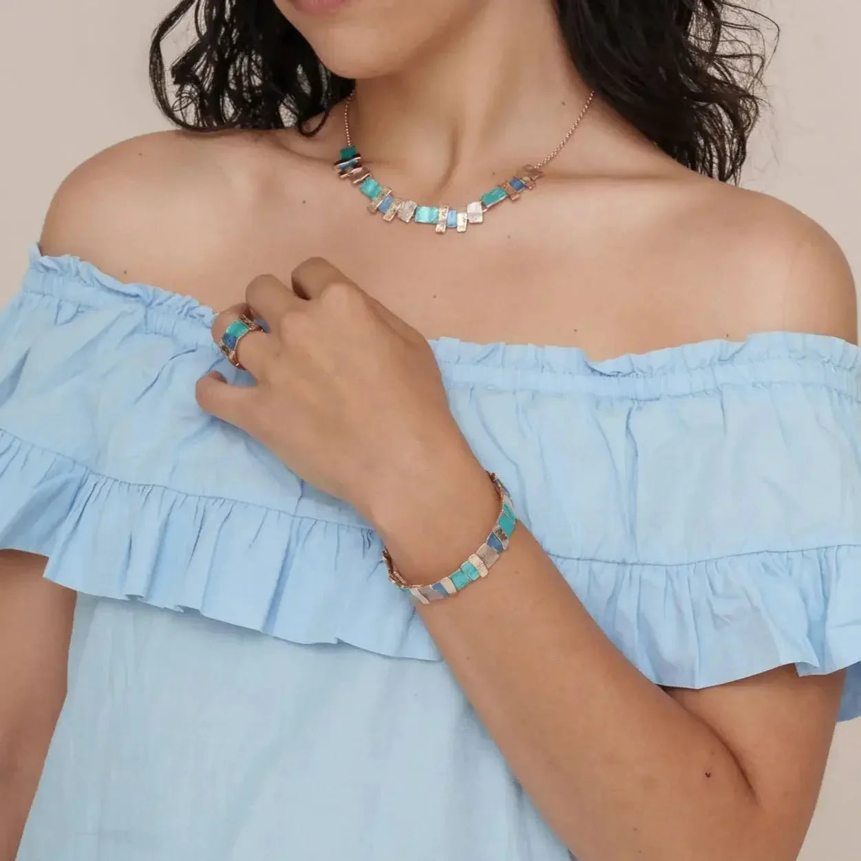 Woman wearing turquoise and gold mosaic bracelet, necklace and ring set with blue off-shoulder top