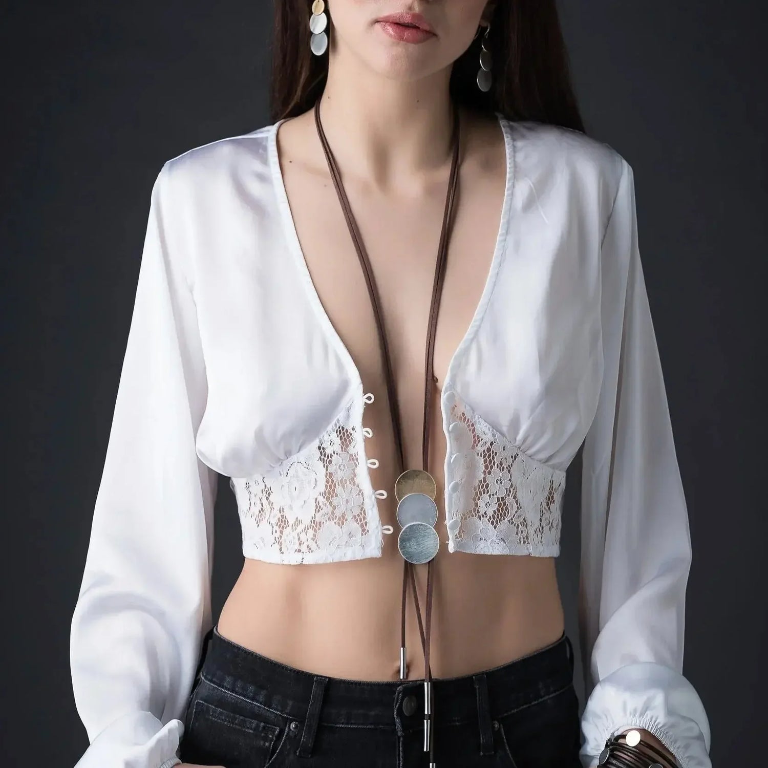 Long necklace with three round metal pendants on woman in white lace crop top and black jeans